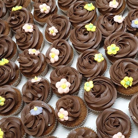 Mange muffinser med sjokolde glasur og en blomstdekor på hver