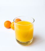 Et glass med appelsinjuice og noen appelsiner som ligger i bakgrunnen