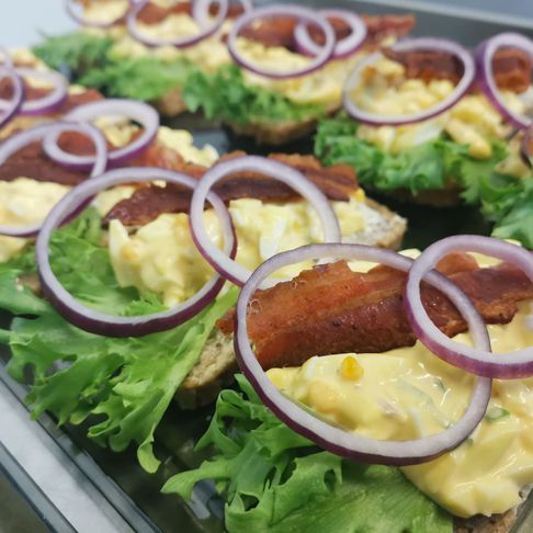 Et brett med påsmurte smørbrød med salat, eggsalat, stekt bacon og rødløk
