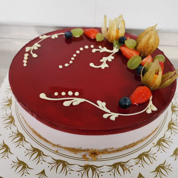 En ostekake med et rødt gelelokk og dekor med glasur og frukt på toppen