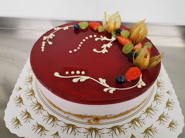 En ostekake med et rødt gelelokk og dekor med glasur og frukt på toppen
