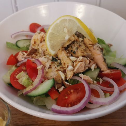 Lakse salat i en hvit bolle med salat, agurk, tomat, paprika, rødløk, stekte lakse biter og sitron