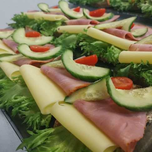 Et brett med påsmurte smørbrød med salat, ost, skinke, agurk og tomat